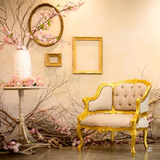 クリーム色の空間に黄金の額縁と椅子・ピンクの花の枝が飾られたスタジオ